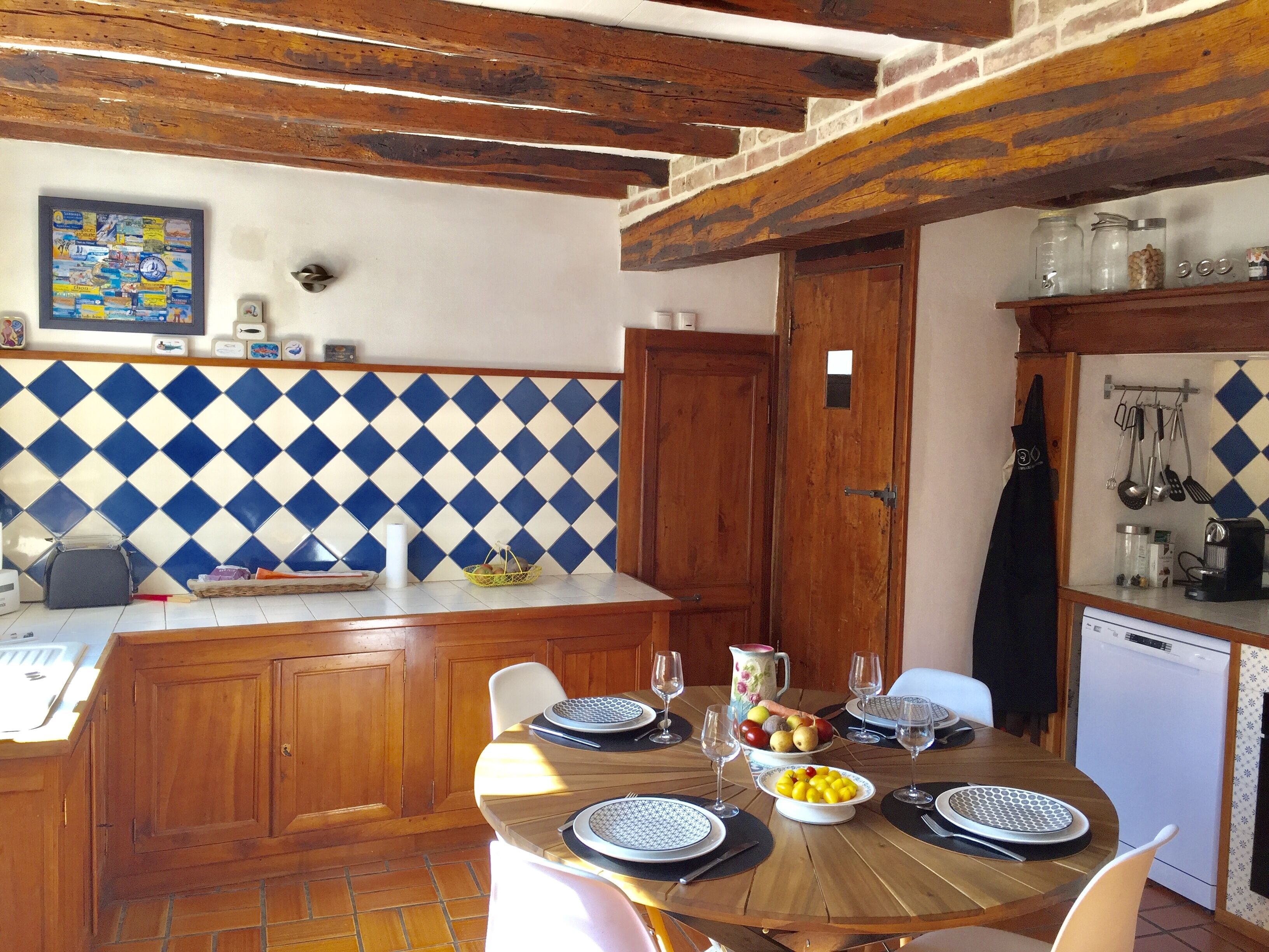 Une cuisine avec une table en bois dressée pour le repas, un plan de travail carrelé et un plafond en bois.