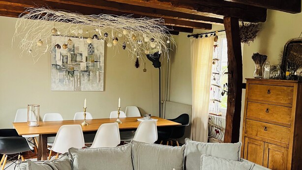 Een gezellige woonkamer met een grijze modulaire bank, een houten eettafel met stoelen en een decoratieve kroonluchter.