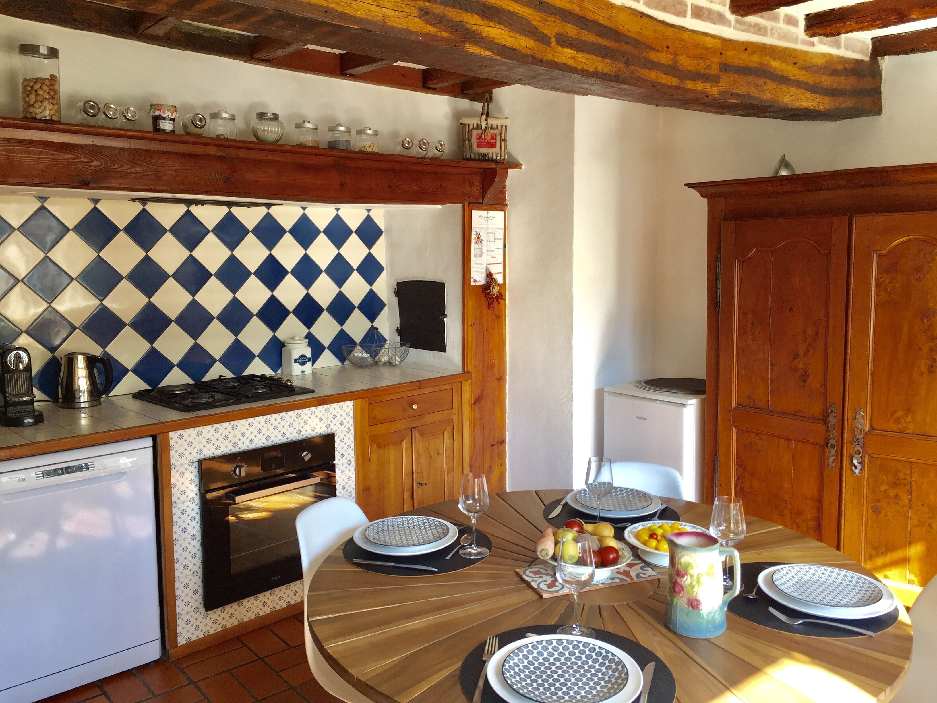 Une cuisine avec un crédence à motifs losanges bleus et blancs, des armoires en bois et un coin repas avec une table ronde mise pour deux personnes.