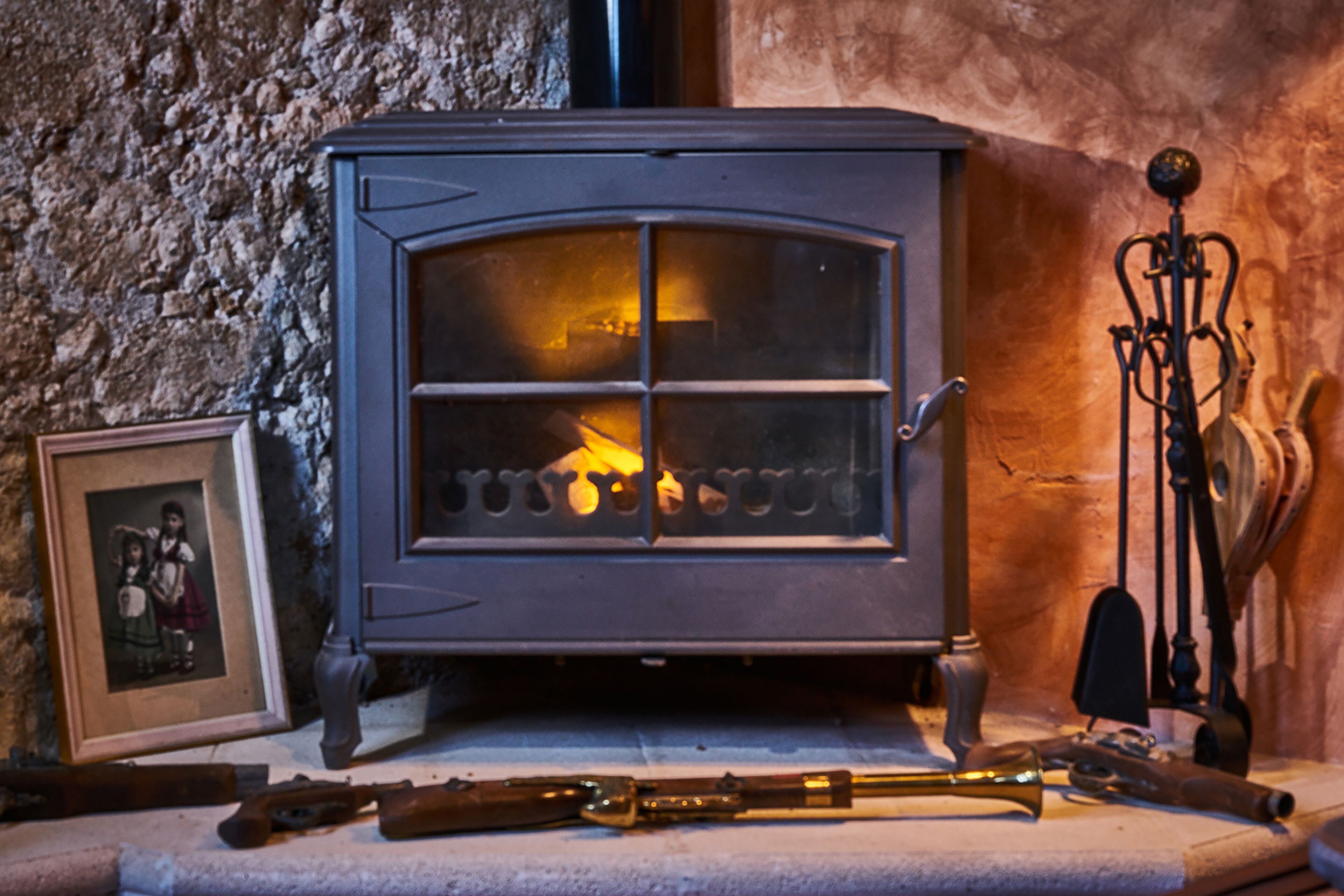 A wood-burning stove with a glass door, a framed picture, and a brass trumpet on the mantel.