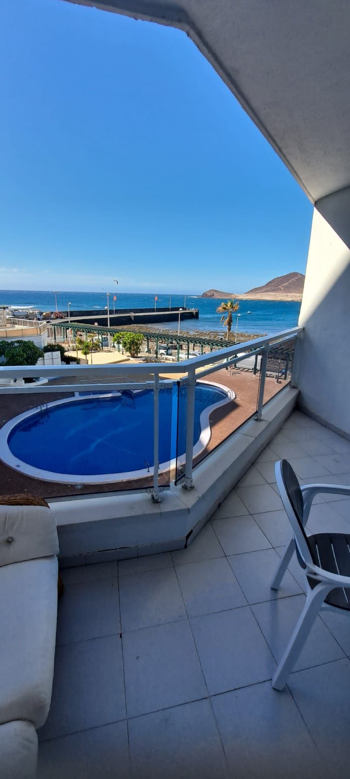 A balcony with a pool, outdoor furniture, and a view of the sea and mountains.