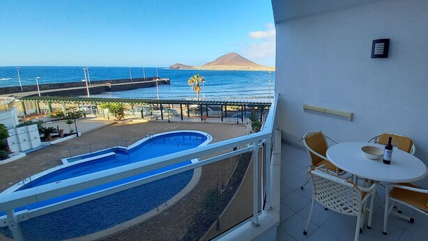 Un balcon avec une piscine, des chaises et une table sur laquelle se trouvent une bouteille et un verre.