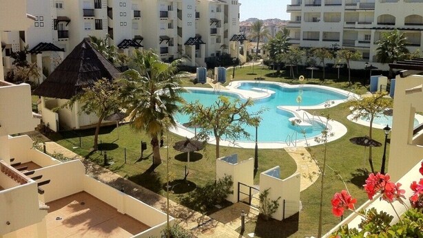 Ein Resort mit mehreren weißen Gebäuden, einem zentralen Pool und umliegender Bepflanzung.