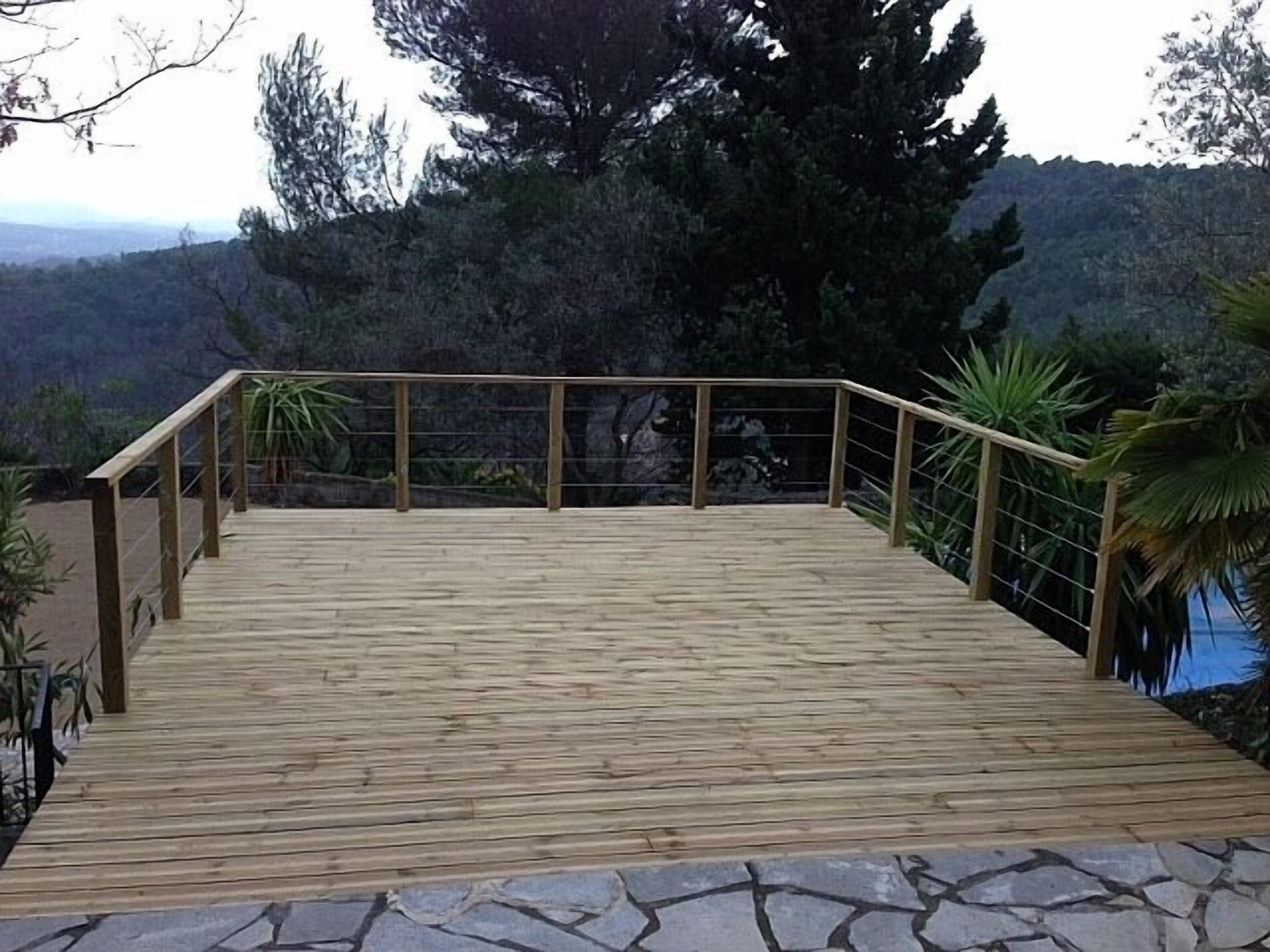 A wooden deck with a stone border, surrounded by trees and a mountainous backdrop.