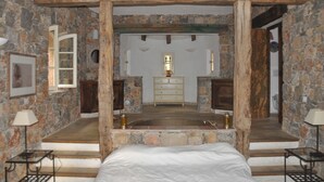 Une chambre aux murs de pierre, dotée d’un grand lit, d’un baldaquin en bois, d’une baignoire en pierre et d’une commode en bois.