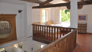 Une pièce avec un balcon en bois, un lit, une fenêtre et un tableau au mur.