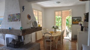 Un coin repas rustique avec un banc en bois, une table avec des chaises et une vue sur l’extérieur grâce à des portes ouvertes.