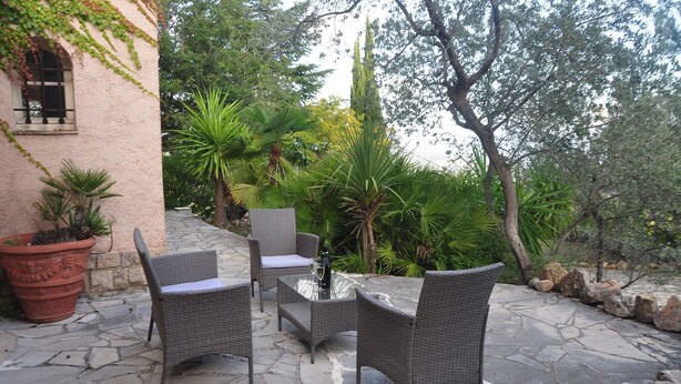 Une terrasse extérieure avec des meubles en osier, une table en pierre et une plante en pot.