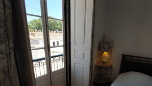 A bedroom with a wooden floor, a bed with white bedding, a nightstand with a lamp, and a door leading to an outdoor balcony. - Town House Within Lagos Castle Walls (Lagos)