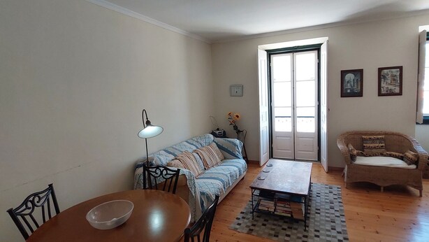 A living room with a wooden floor, a dining table with chairs, a sofa, a patterned rug, and a door leading outside. - Town House Within Lagos Castle Walls (Lagos)