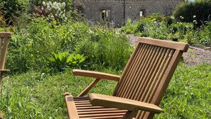 A wooden chair in a lush garden with a stone building in the background. - Beautiful Stone Cottage - A Unique Rural Retreat In The Scottish Borders (Duns)