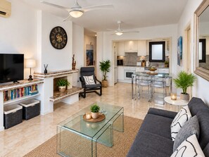 Een moderne woonkamer met een televisie, boekenkasten, een glazen salontafel, een bank en een eethoek met stoelen en een tafel.