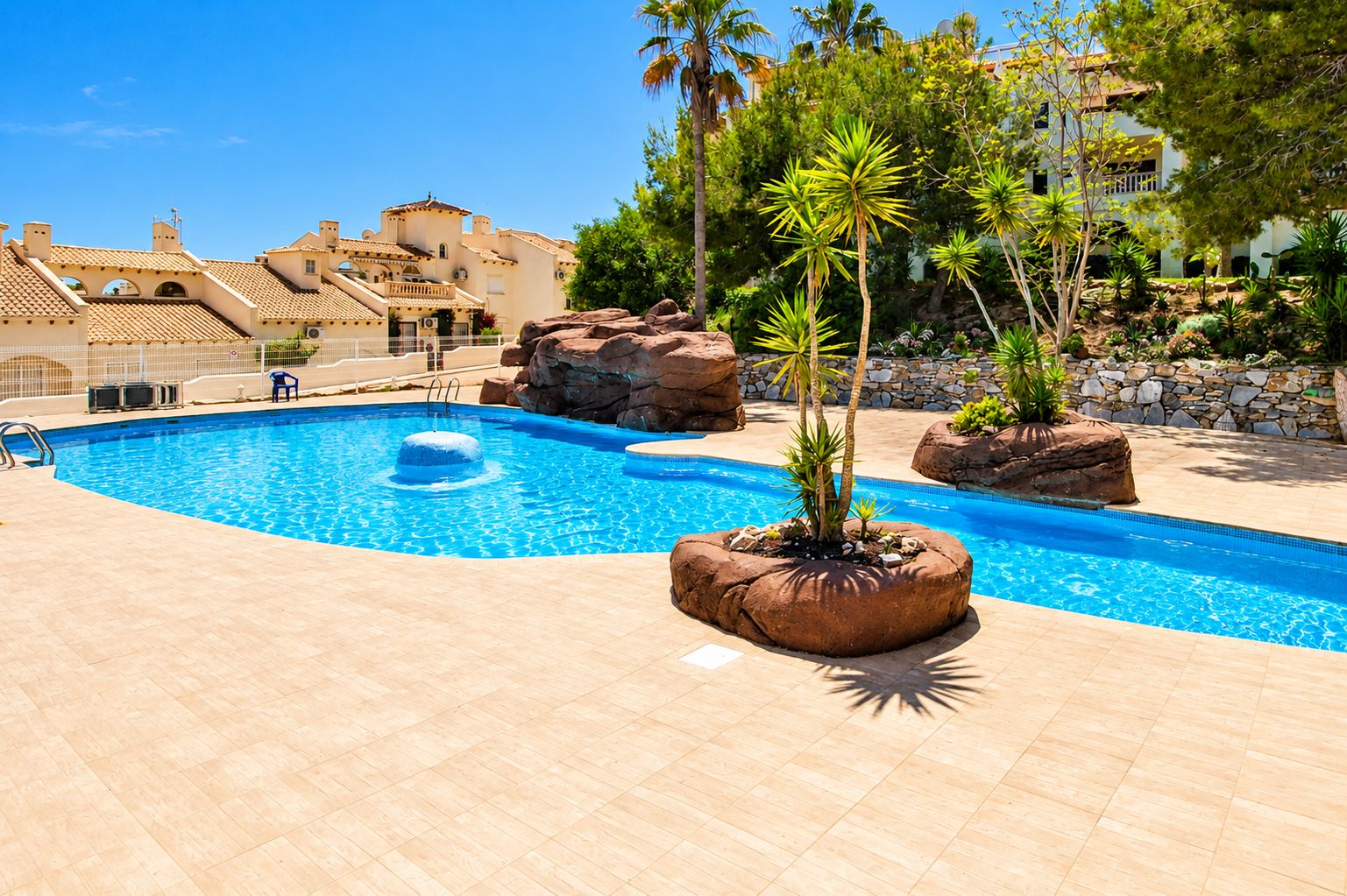 Una piscina con un'acqua cristallina e azzurra, circondata da una terrazza piastrellata e formazioni rocciose.