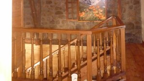 Interior de madera con una escalera de madera, una pared de piedra y un cuadro de un paisaje montañoso.