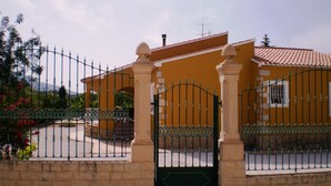 A gated entrance with a yellow building, a stone wall, and a metal gate.