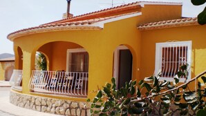 A yellow building with a stone base, a balcony with metal railings, and a window with bars.