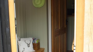 Een houten deur die uitkomt op een gang met een bank, een groene hoed en een doos boeken.