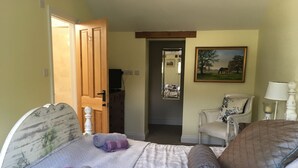 Een slaapkamer met een bed, een stoel, een schilderij en een deur naar een andere kamer.