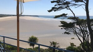 A beach view from a balcony with a large umbrella, a railing, and some trees.