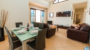 A dining area with a table set for four, a sofa, and a television in the background. - Modern & bright, only a short walk into the town centre, A/C & heated pool (Playa Blanca)