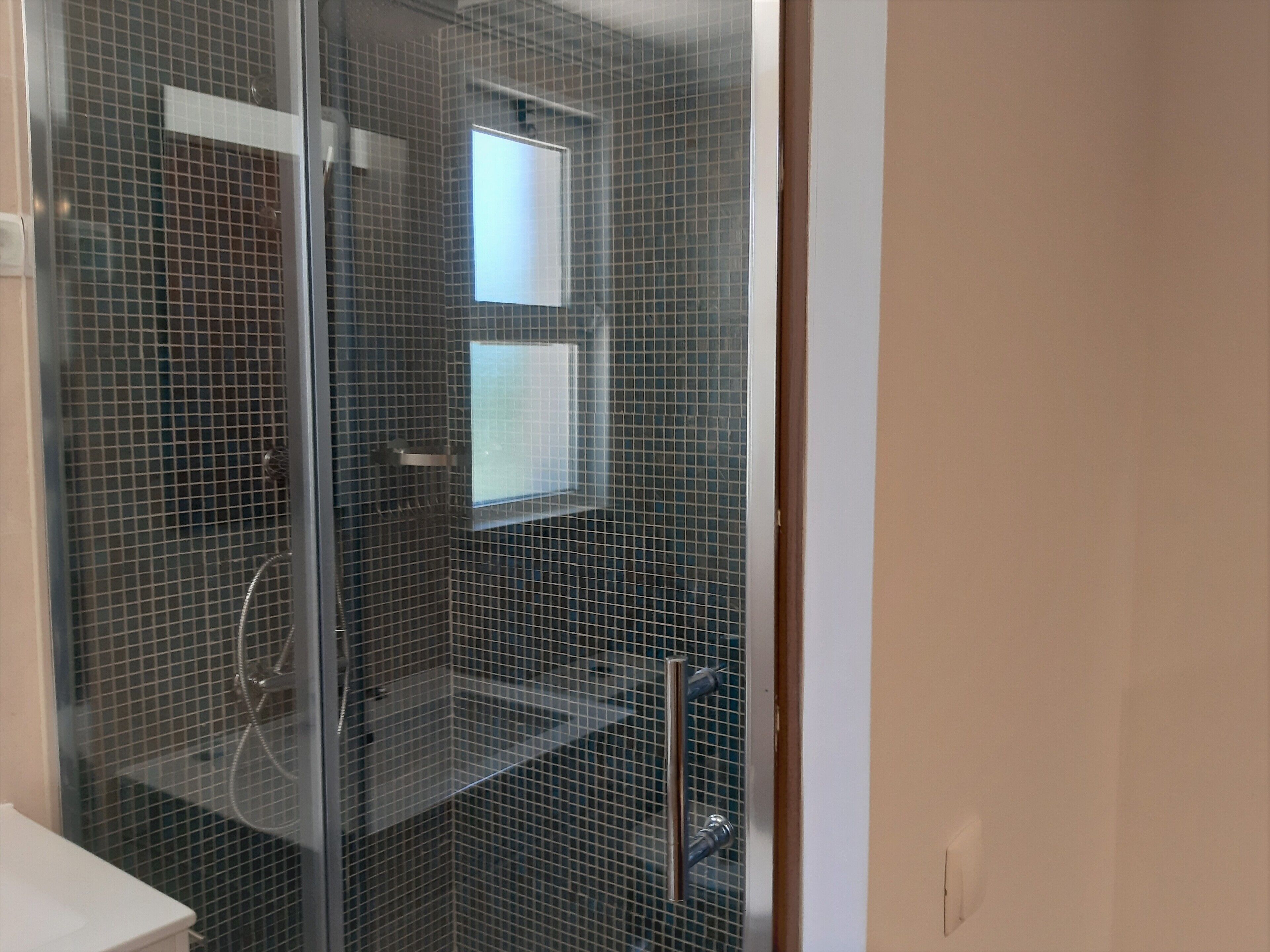 A shower area with a glass door, tiled walls, and a visible shower head.