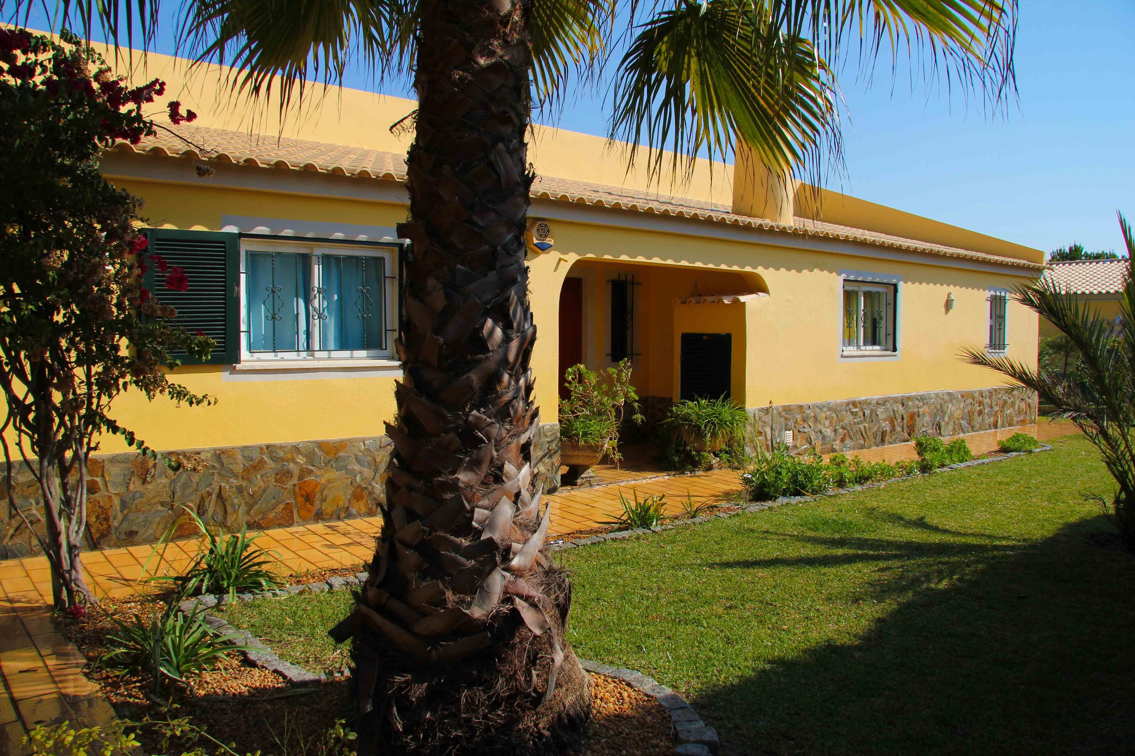A yellow building with a stone foundation, a palm tree, and a well-maintained garden.
