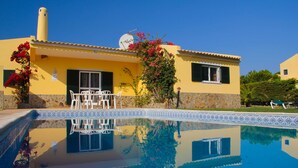 Una villa gialla con piscina, mobili da esterno e antenna parabolica.