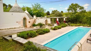 Una piscina con un muro de piedra y un edificio pequeño con techo cónico.