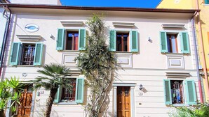 A building with multiple windows and doors, some with shutters, and a small bench in front. - Franco House in the Old Town (Marina di Campo)