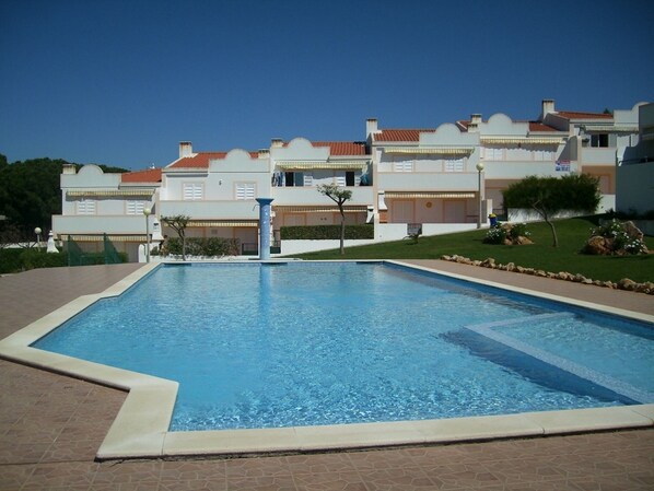 A swimming pool with a tiled deck, surrounded by a landscaped garden and a row of buildings with balconies. - Apartment with air conditioning, quiet residence with pool, close to beaches (PORCHES)