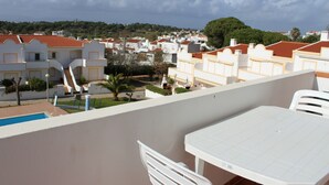 En balkon med pool, hvide møbler og udsigt over et boligområde med røde tage.