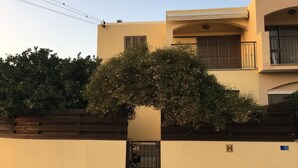 Un bâtiment à deux étages avec une façade beige, une clôture en bois et un arbre devant.