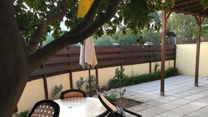 Une terrasse avec une table ronde et des chaises, une pergola en bois et un petit arbre.