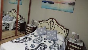 A bedroom with a bed, bedside tables, a mirror, and a painting of a sunset over water.