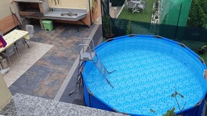 A backyard with a blue above-ground pool, a barbecue grill, and a dining area.