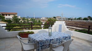 A terrace with a table and chairs, overlooking a coastal area with houses and greenery. - beautiful apartment in villa, private beach with umbrellas and sunbeds (Marzamemi)