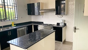 A kitchen with a central island, a stove, a coffee maker, and a dishwasher. - 6 BEDROOM HOUSE  IN COMMUNITY 20, GREATER ACCRA , TEMA OFF THE SPINTEX ROAD (Tema New Town)