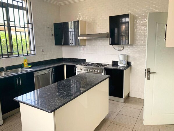 A kitchen with a central island, a stove, a coffee maker, and a dishwasher.