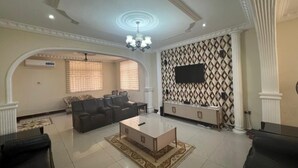A spacious living room with a large sofa set, a coffee table, and a TV mounted on the wall. - 6 BEDROOM HOUSE  IN COMMUNITY 20, GREATER ACCRA , TEMA OFF THE SPINTEX ROAD (Tema New Town)