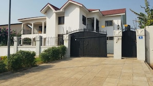 A two-story house with a gated entrance, a balcony, and a red roof. - 6 BEDROOM HOUSE  IN COMMUNITY 20, GREATER ACCRA , TEMA OFF THE SPINTEX ROAD (Tema New Town)