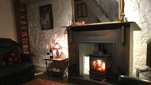 A cozy living room with a fireplace, a leather armchair, a coffee table with a lamp, and a bookshelf. - Traditional Stone Cottage (Ammanford)