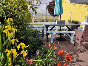 Eine Holzterrasse mit Tisch und Stühlen, umgeben von verschiedenen Blumen und Grünpflanzen.