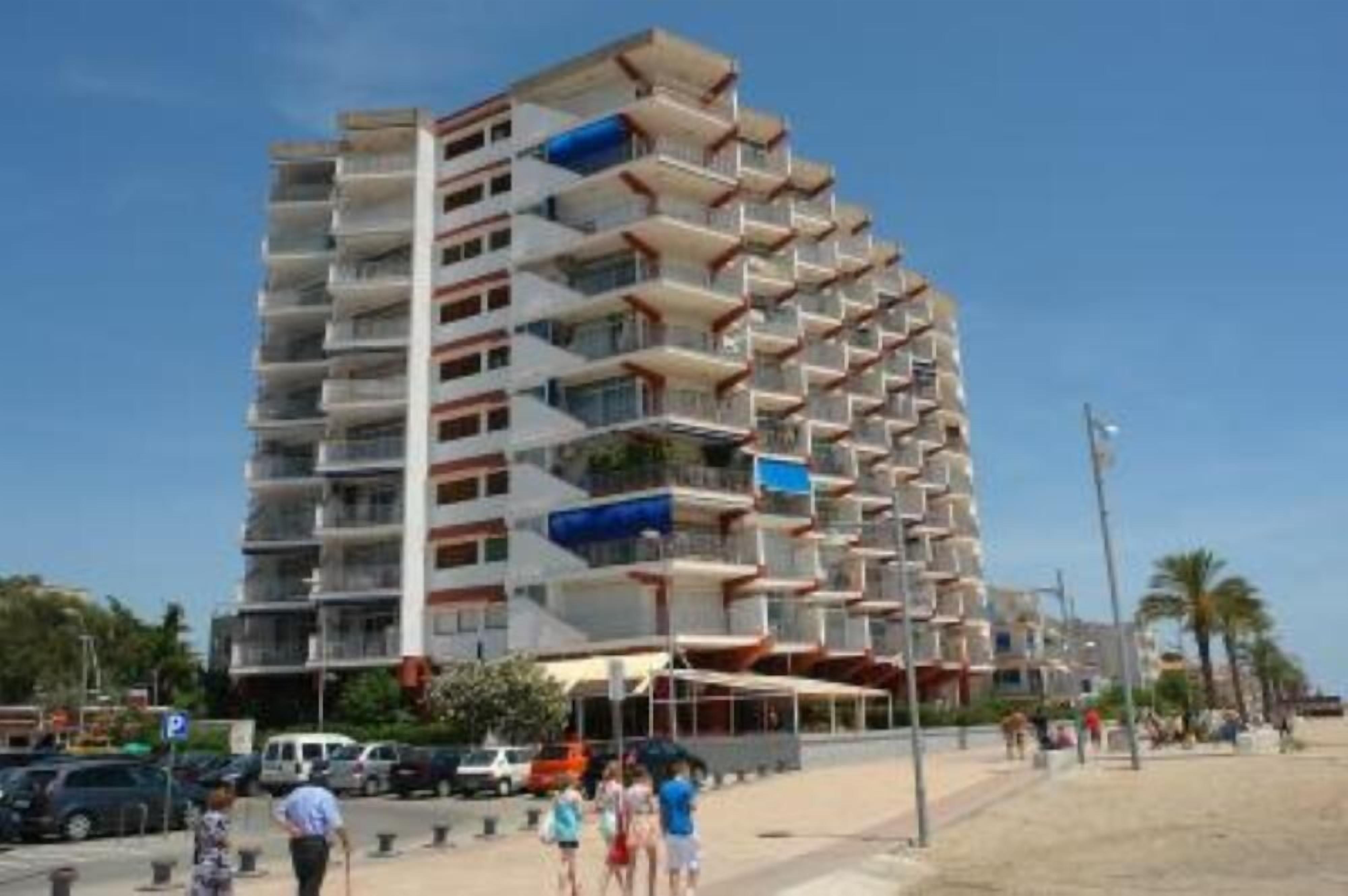 A multi-story hotel with balconies, located near a beach.