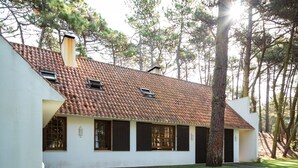 A white building with a tiled roof, multiple windows, and a grassy lawn. - Garden, near the beach, car essential (Banzão)
