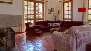 A cozy living room with a red sofa, a wooden coffee table, and a patterned throw on a bed. - Garden, near the beach, car essential (Banzão)