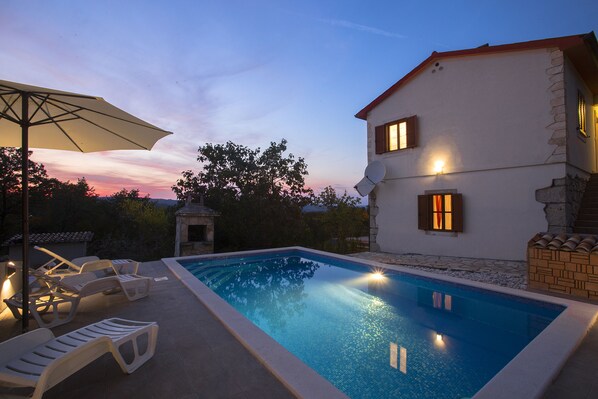 A swimming pool with lounge chairs and an umbrella, surrounded by a house with stone walls and a red roof. - Seaside Bliss: Unwind in Your Exclusive Summer Rental Paradise (Labin)