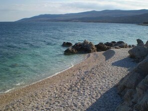 A pebble beach with clear water and rocky outcrops. - Seaside Bliss: Unwind in Your Exclusive Summer Rental Paradise (Labin)