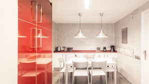 A modern kitchen with white cabinets, a red accent wall, and pendant lighting.