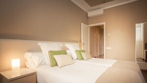 A neatly made bed with white and green pillows, a bedside lamp, and a nightstand with drawers.