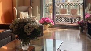 A room with a glass table, a chair, a sofa with cushions, and a balcony with a view of buildings.